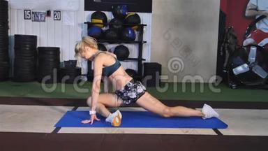 女人在健身房里坐在垫子上伸腿。 女人在健身房热身，背景是设备。